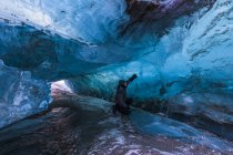 Mann untersucht klares blaues Eis im Tunnel unter der Oberfläche des schwarzen Stromschnellen-Gletschers im Winter, Alaska, Vereinigte Staaten von Amerika — Stockfoto