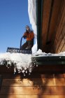 Young woman removing snow from the roof of house — Stock Photo