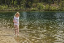 Junges Mädchen spielt im Wasser an einem Sandstrand am Fluss im Wald — Stockfoto