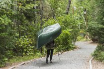 Una joven que lleva una canoa verde en su cabeza por un sendero; Ontario, Canadá - foto de stock