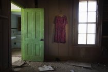 Quarto dentro de uma antiga casa abandonada com uma porta verde aberta e um vestido velho pendurado na parede; Estados Unidos da América — Fotografia de Stock