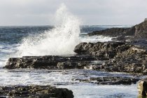 Хвиля врізається в скелясте узбережжя з хмарним небом — стокове фото