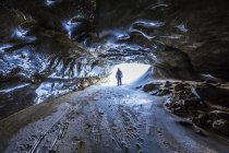 A man stands in the entrance to a lengthy tunnel beneath the ice of Castner Glacier in the Alaska Range; Alaska, United States of America — Stock Photo