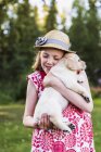 A young girl wearing a sundress and hat holding a Labrador puppy in her arms; Anchorage, Alaska, United States of America — Stock Photo