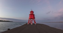 Red lighthouse along coast at sunset — Stock Photo