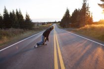 Visão traseira do jovem skate na estrada ao entardecer — Fotografia de Stock