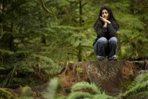 Jovem mulher adulta sentada em grande toco na antiga floresta verde — Fotografia de Stock