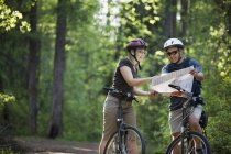 Couple caucasien sur les vélos en regardant la carte à la nature — Photo de stock