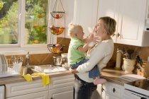 Madre caucásica e hija bebé abrazándose en la cocina y divirtiéndose - foto de stock