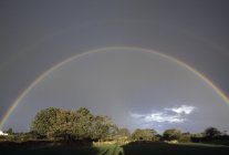 Rainbow over trees with field — Stock Photo