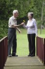 Heureux vieux couple caucasien partage de fleurs sur pont — Photo de stock