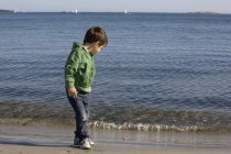 Хлопчик стоїть на пляжі проти хвилясті води — стокове фото