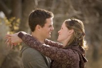 Atractiva pareja feliz abrazándose y mirándose en el parque de otoño - foto de stock