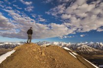 Randonneur masculin debout sur le sommet de la colline contre le ciel nuageux pendant aytime — Photo de stock