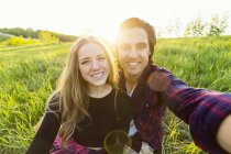Jeune couple romantique faisant sefie à l'extérieur sur l'herbe verte et souriant à la caméra — Photo de stock