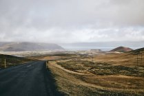 Un camino de asfalto a lo largo de la costa bajo un cielo nublado; Islandia - foto de stock