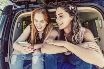 Two girls sitting in car and looking into phone — Stock Photo