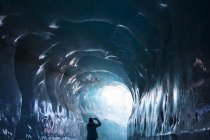 Rear view of woman standing in ice tunnel and making photo on smartphone — Stock Photo