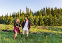 Счастливая пара, идущая по траве в лесу и держащаяся за руки — стоковое фото