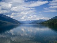 Calm blue lake water and hills under cloudy sky on background — Stock Photo