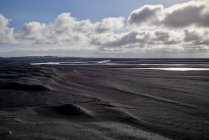 Ein Fluss, der durch ein Flussbett aus schwarzem Sand fließt, mit Bergen in der Ferne; Island — Stockfoto
