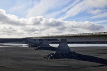 Un puente que cruza un río que atraviesa el cauce de arena negra; Islandia - foto de stock