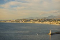 Un faro al final del muelle y a lo largo de la costa de la Riviera francesa; Niza, Costa Azul, Francia - foto de stock