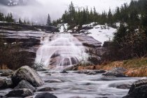 Wasserfall auf Felsplatte in der Nähe des Nellie-Juan-Gletschers an bewölkten Tagen mit Schnee; weißer, alaska, vereinigte staaten von amerika — Stockfoto