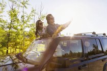 Yound couple standing at car with flap top and making selfie against trees — Stock Photo