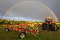 Vista del tractor trabajando en campo con herramienta y arco iris sobre fondo - foto de stock