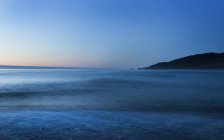 Tranquil sea water and hill on background at sunset — Stock Photo
