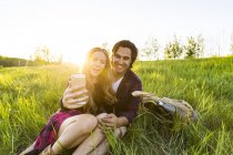 Young couple sitting on green grass and making selfie with smartphone — Stock Photo