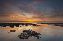 View of sunset over shore with stones against water of calm sea — Stock Photo