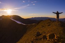 Man standing on mount top with arms outstretched against sun — Stock Photo