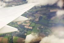 Partial View of aircraft wing flying over village with green field during daytime — Stock Photo