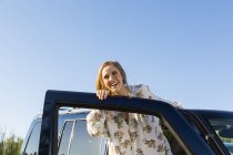 Feliz sorrindo mulher apoiando-se na porta aberta do carro — Fotografia de Stock