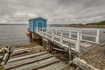 Small wooden blue barn over water on pier  and hills on background — Stock Photo