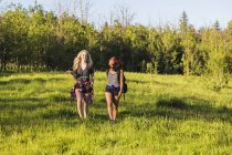 Two happy girls walking over grass in forest during daytime — Stock Photo