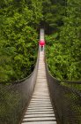 Mulher com um guarda-chuva em forma de coração vermelho atravessando a ponte de suspensão Lynn Canyon, North Vancouver; Vancouver, British Columbia, Canadá — Fotografia de Stock