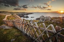 Старый деревянный забор на поле с зеленой травой и спокойной морской водой с каменистым берегом — стоковое фото