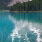 Деревья и склоны отражаются в спокойной голубой воде озера в дневное время — стоковое фото