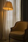 Uma lâmpada de assoalho iluminada ao lado de uma cadeira e de uma janela; Cannes, Cote D 'azur, França — Fotografia de Stock