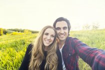 Heureux couple romantique faisant sefie à l'extérieur sur l'herbe verte et souriant à la caméra — Photo de stock