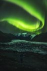 Green northern light over mountains and lake water at night — Stock Photo