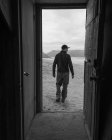 Homem caminhando e olhando para longe com montanhas no fundo, vista da porta, imagem em preto e branco — Fotografia de Stock