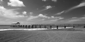 Black and white picture of wooden pier over sea water under cloudy sky — Stock Photo