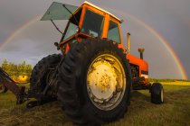 Vue à angle bas du tracteur travaillant sur le terrain avec outil et arc-en-ciel sur fond — Photo de stock