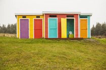 Portas de madeira coloridas em uma fileira em pequenas barracas de madeira sobre campo de grama verde — Fotografia de Stock