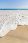 Eau passant sur la plage de sable et l'eau bleue claire sur le fond — Photo de stock