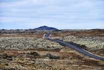 Uma estrada atravessa uma paisagem estéril com uma montanha à distância, Península de Snaefellsnes; Islândia — Fotografia de Stock